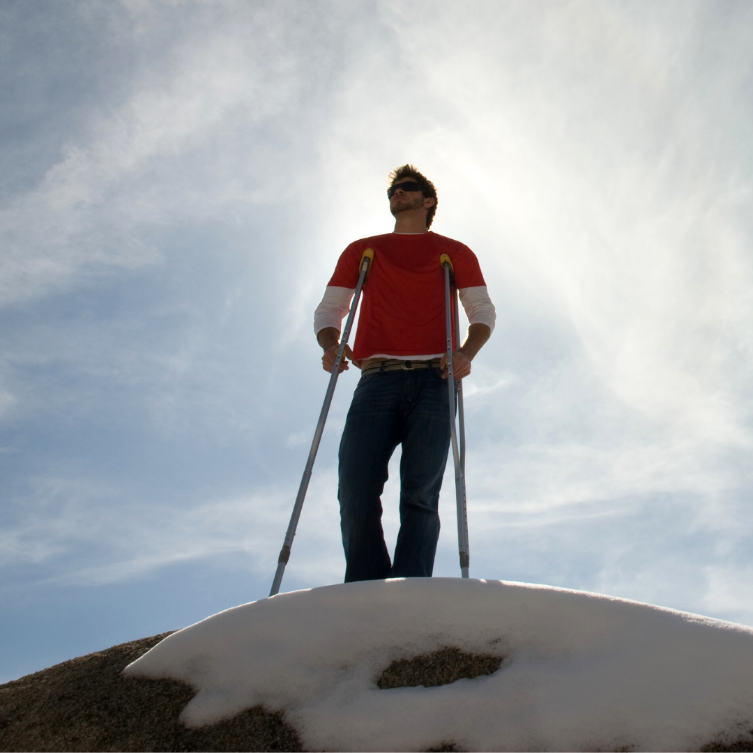 Man on crutches at the top of a mountain